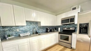 A modern kitchen with white cabinets, a blue-tiled backsplash, stainless steel appliances, and wooden flooring. - Miami 3BR | Walk to LoanDepot Park | Patio (Miami)