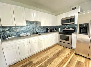 A modern kitchen with white cabinets, a blue-tiled backsplash, stainless steel appliances, and wooden flooring. - Miami 3BR | Walk to LoanDepot Park | Patio (Miami)