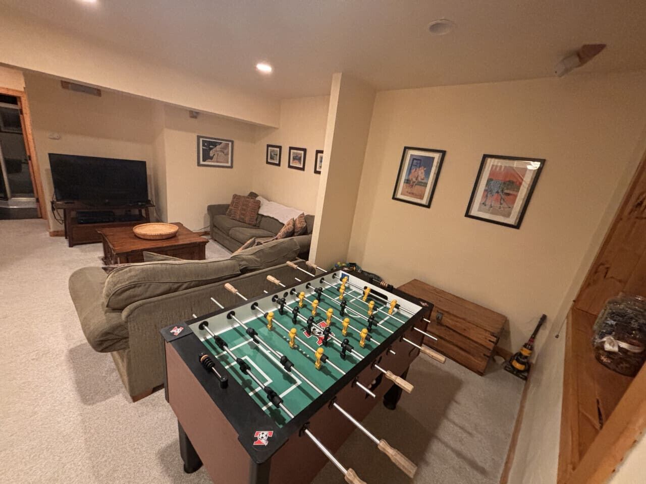 Une pièce avec une table de baby-foot, un canapé, un téléviseur et des tableaux encadrés au mur.