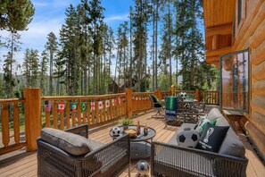 A wooden deck with outdoor furniture, a dining table, and a view of tall trees.