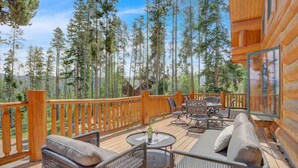 A wooden deck with outdoor furniture, surrounded by tall trees. - Indulge | Majestic Views | Tipi | Hot Tub - Sauna (Winter Park)