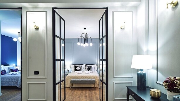 Une chambre à coucher avec un lit, une table de chevet, une lampe et une vue sur une autre pièce.