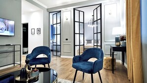 Un salon moderne avec deux fauteuils bleus, une table basse en verre et un téléviseur fixé au mur.