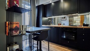 Une cuisine moderne avec des meubles de couleur sombre, un plan de travail en bois et un four encastré. On y trouve un tabouret de bar et une étagère remplie de livres.