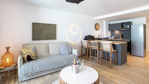 A modern living room with a sofa, a dining area with chairs, a kitchen with a refrigerator, and a pendant light.