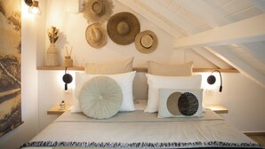 A bedroom with a bed, pillows, a nightstand, a wall-mounted hat rack, and a painting.