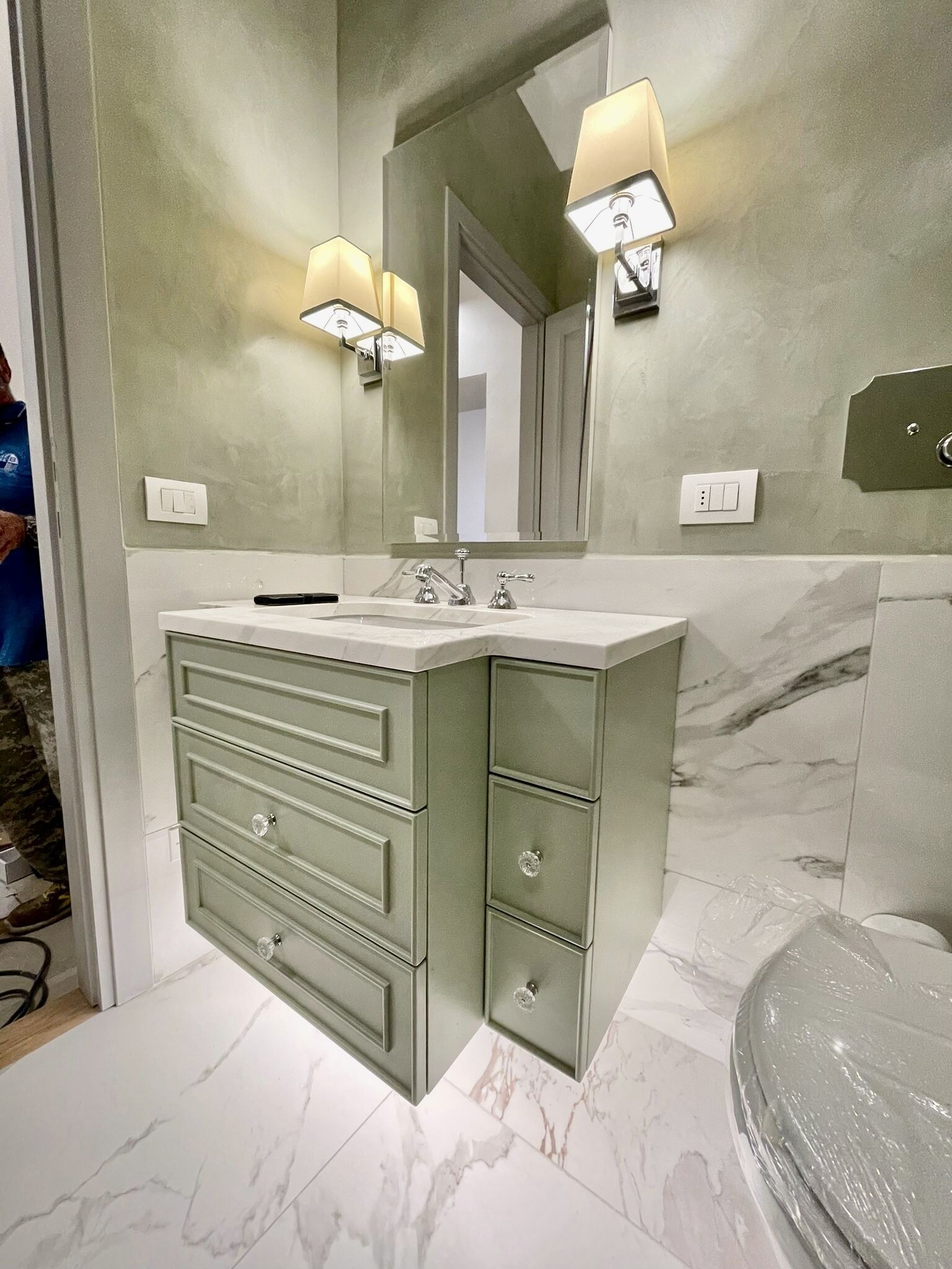 A bathroom with a marble vanity, a large mirror, and wall-mounted lights.