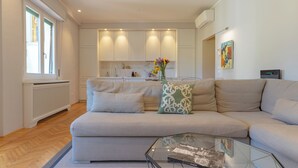 A modern living room with a sofa, a glass coffee table, and a kitchen in the background. - Steps to Ponte Vecchio.3BR/3BA+terrace w view of Pitti Palace (Firenze)
