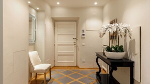 A hallway with a white door, a white chair, a black console table with a white orchid pot, and a patterned floor. - Steps to Ponte Vecchio.3BR/3BA+terrace w view of Pitti Palace (Firenze)