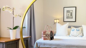 A hotel room with a bed, a bedside table with a potted plant, a mirror, a framed picture on the wall, and a decorative bag on the bed. - Steps to Ponte Vecchio.3BR/3BA+terrace w view of Pitti Palace (Firenze)