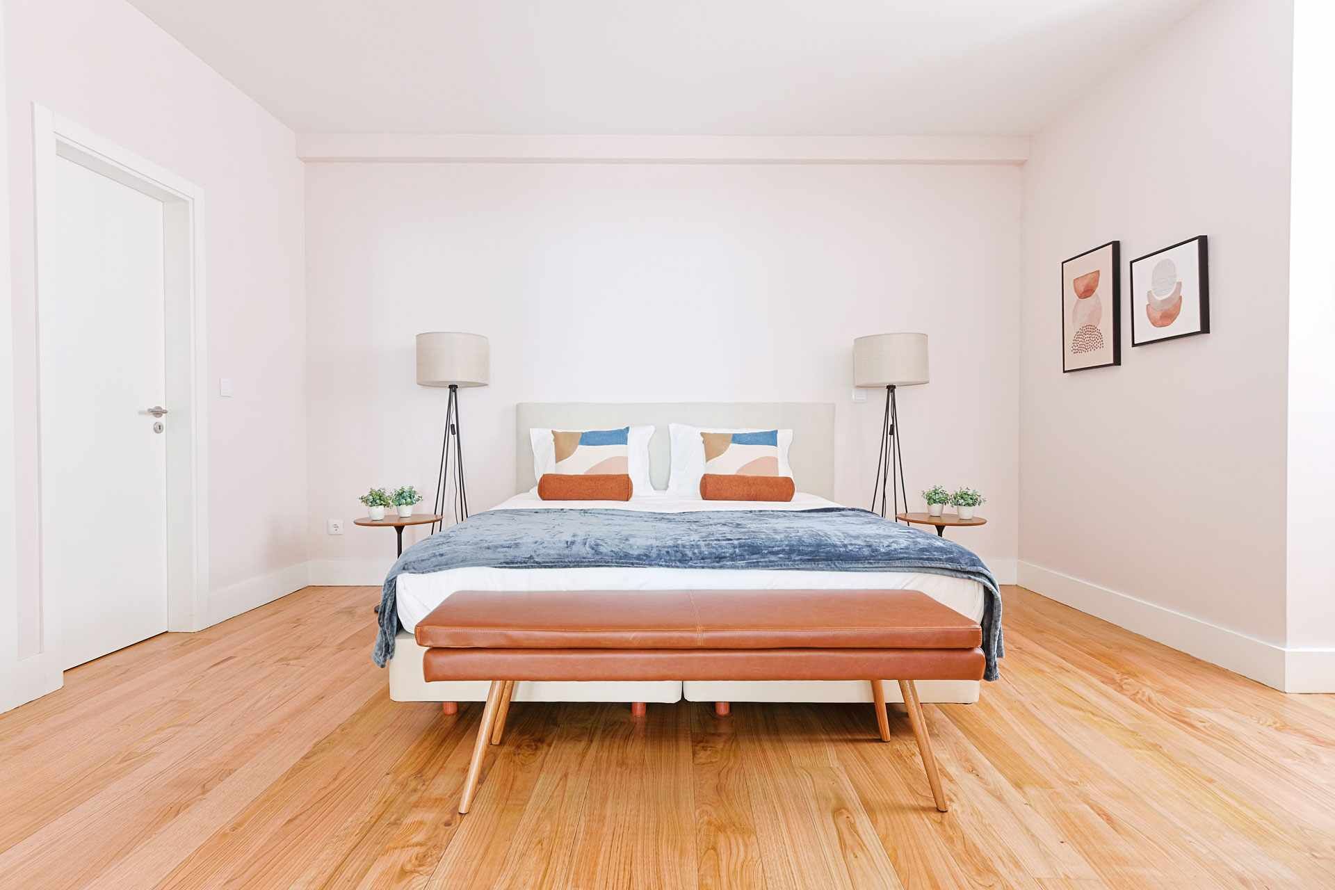 A bedroom with a bed, two bedside tables, a floor lamp, a headboard with a geometric design, and two framed pictures on the wall.