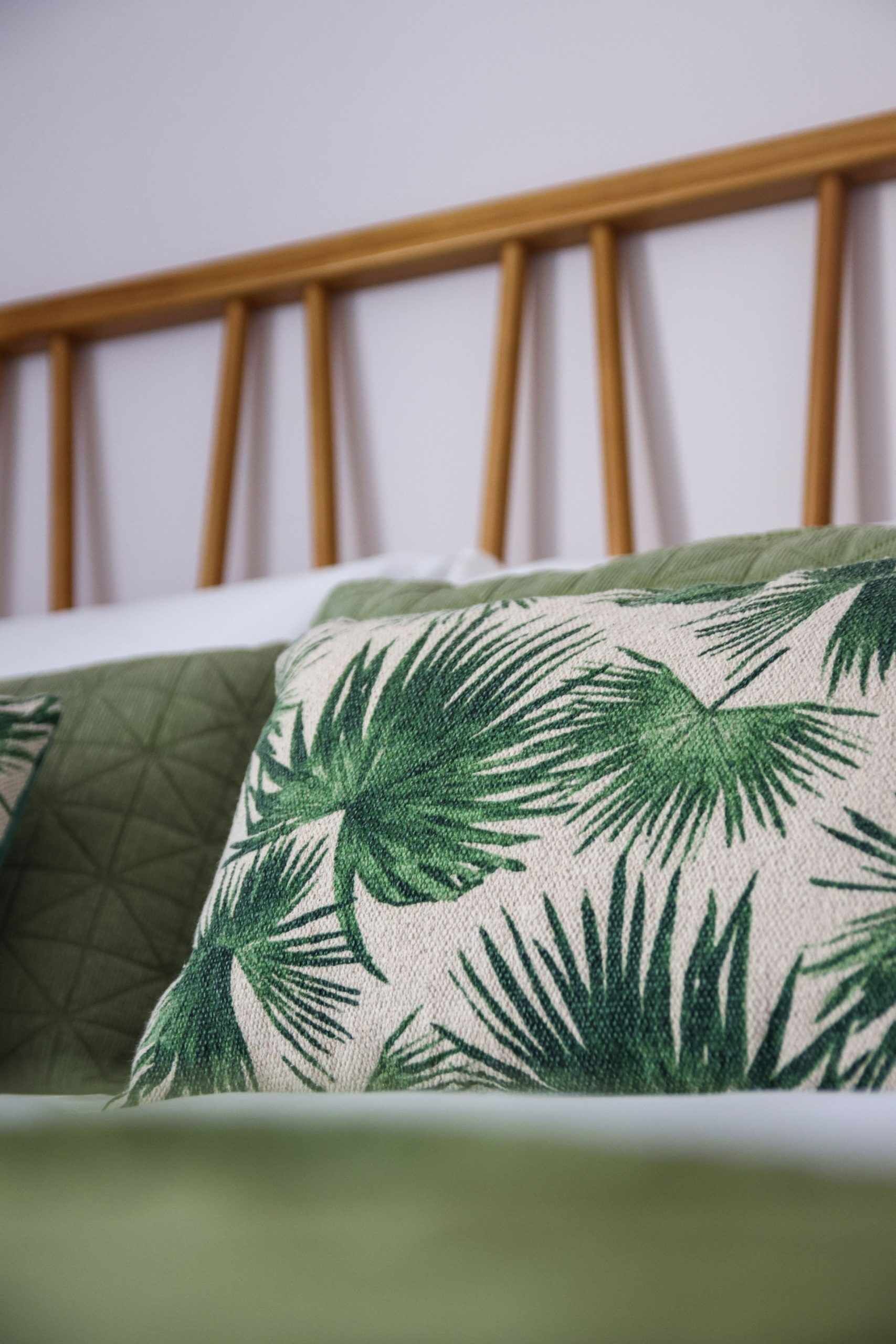 Ein Bett mit grünen und beigen Kissen mit Palmenblattmuster.