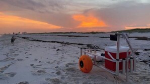 Escena de playa con huellas, un puesto de salvavidas y una puesta de sol.