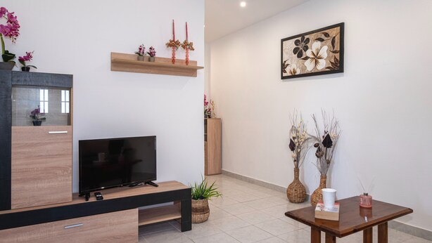 A modern living room with a flat-screen TV, wooden entertainment unit, and a dining table with a vase and book. - Laurel LK Apt in Kremasti Near Airport Rhodes (Rhodes)