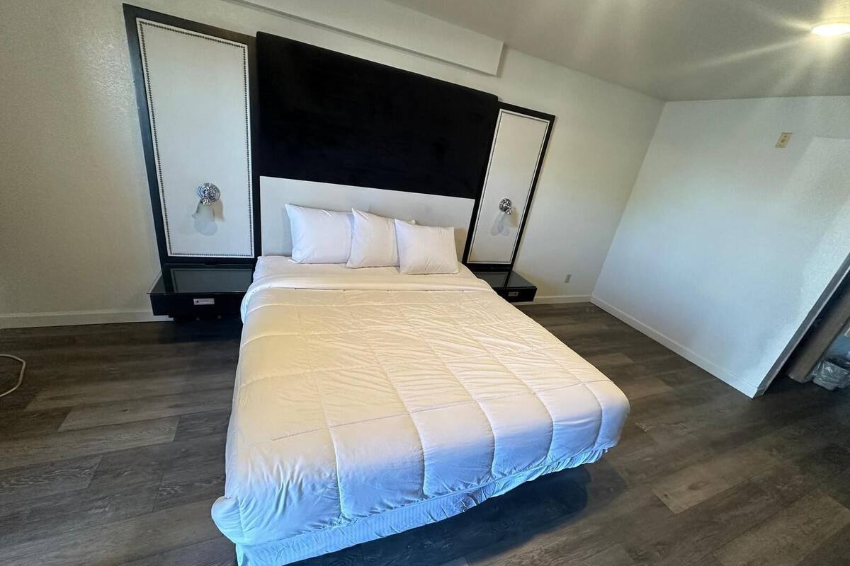 A large bed with a white quilted bedspread and a black headboard. There are two bedside tables with lamps, and a large mirror on the wall.