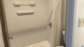 Un baño con cabina de ducha, inodoro y suelo de baldosas.