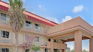 A multi-story hotel with a red roof, a covered parking area, and a palm tree in the foreground. - GO2 Inn & Suites by Relianse  (El Paso)