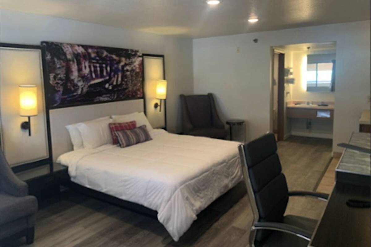 A hotel room with a bed, two wall-mounted lamps, a chair, a desk, and a painting on the wall.