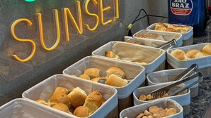 A buffet area with a neon sign reading "GREEN SUNSET" and various food items in containers. - Melhores Flats (João Pessoa)