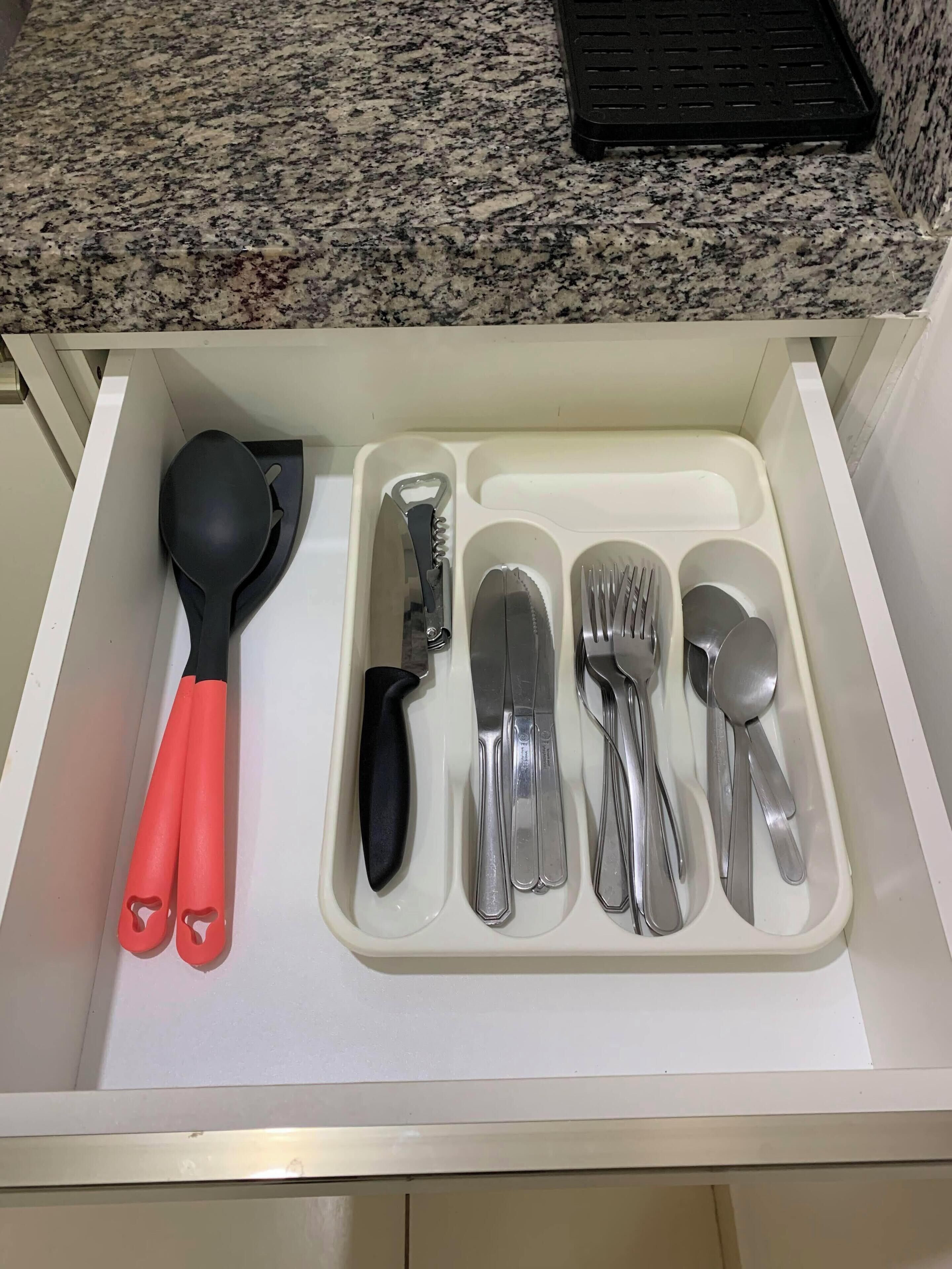 Un cajón con un juego de utensilios de cocina, incluyendo una espátula, un cuchillo y varias cucharas.