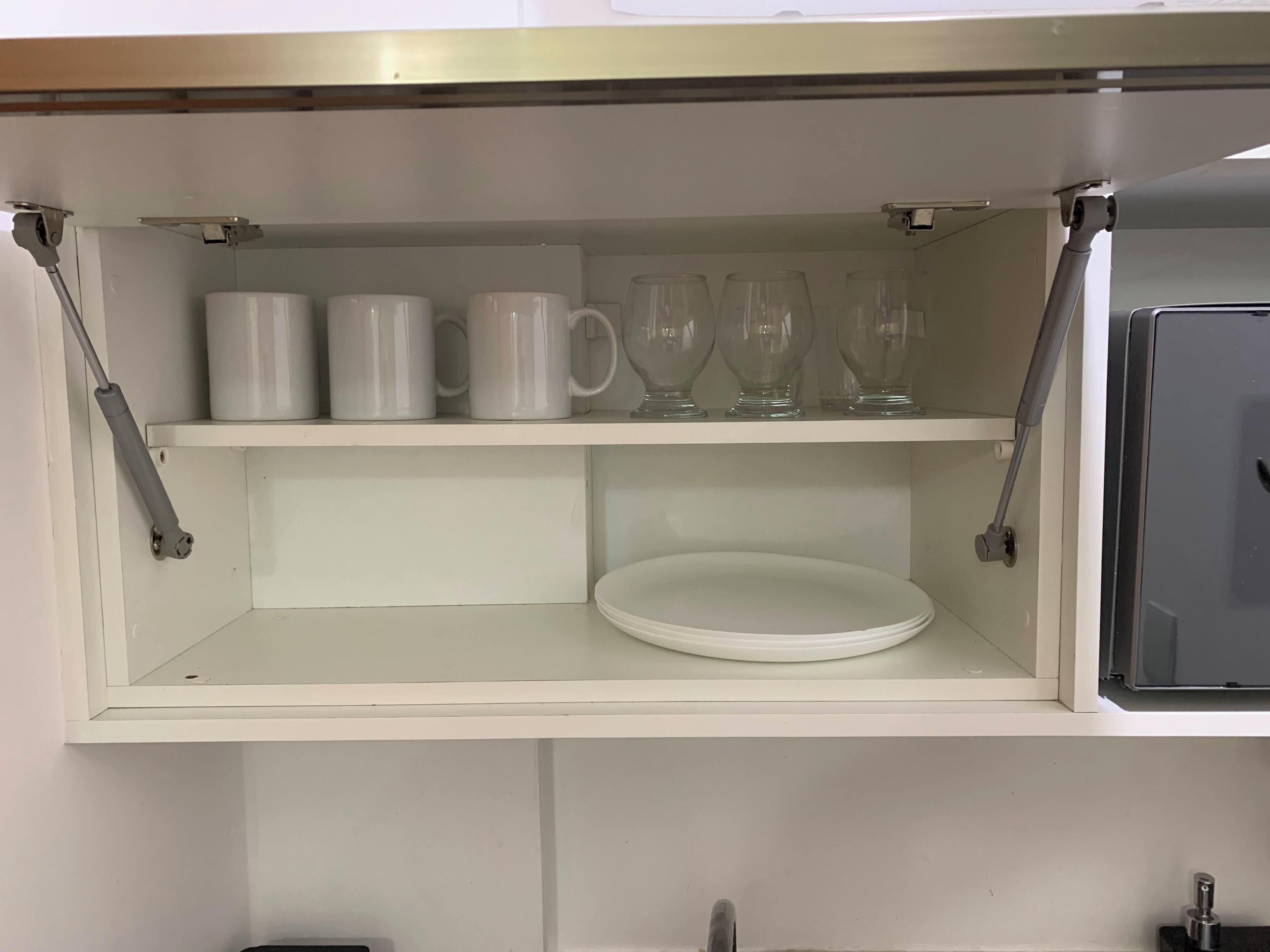 A white shelf with white mugs and clear glassware.