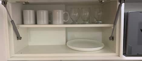 A white shelf with white mugs and clear glassware.