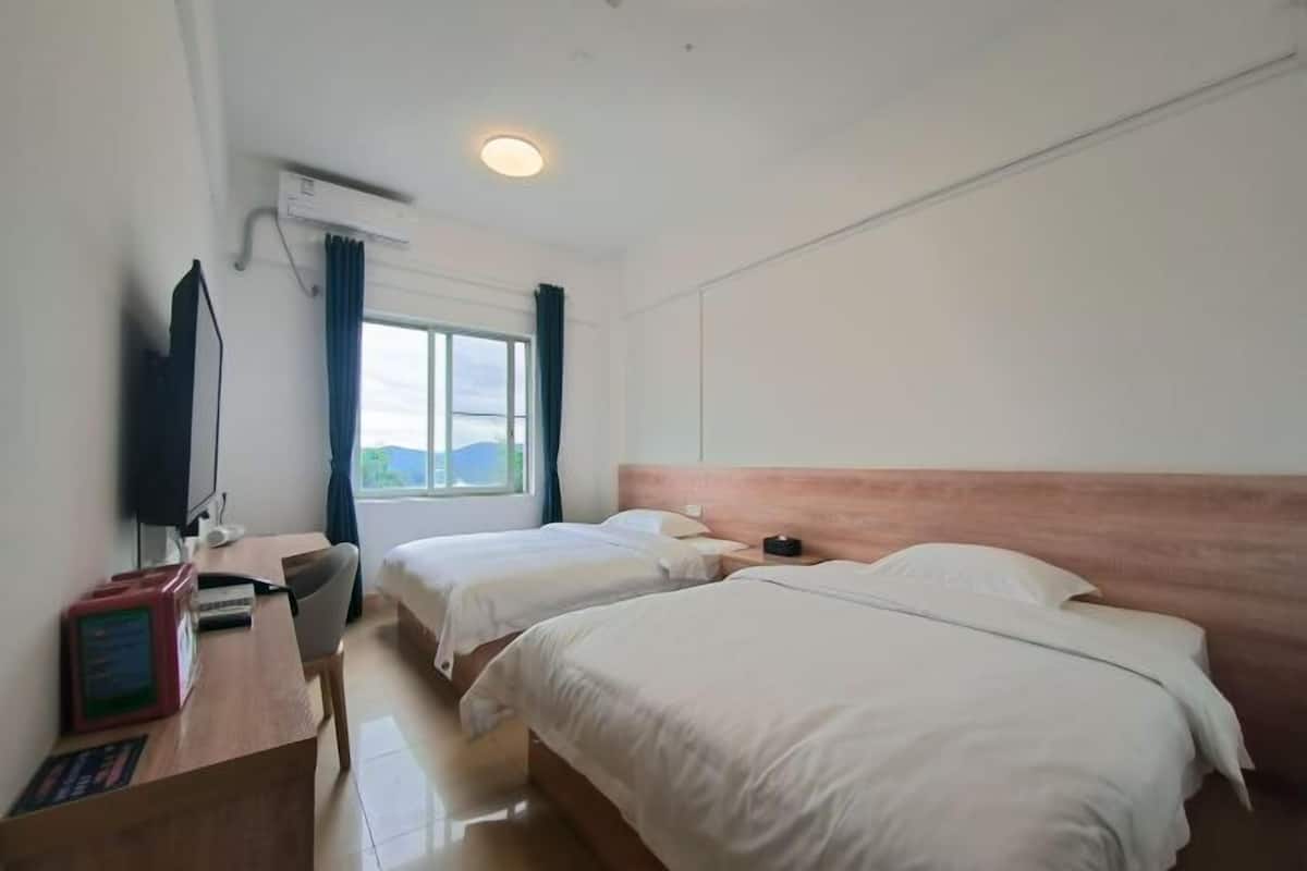 Une chambre d’hôtel avec deux lits, un bureau avec un ordinateur, une télévision et une fenêtre avec des rideaux.