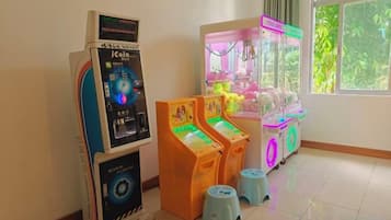 Una habitación con una máquina de juegos con monedas, dos máquinas de grúa y una ventana con vistas a zonas verdes.