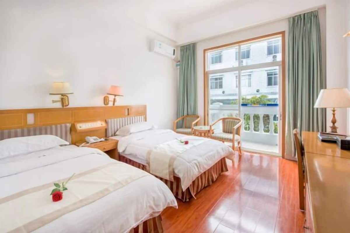 Une chambre d’hôtel avec deux lits, une tête de lit en bois, une petite table, une chaise et une fenêtre avec des rideaux.