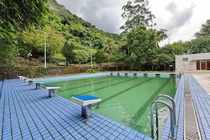 A swimming pool with a tiled deck, benches, and a building in the background. - Huguang Holiday Hotel (Guangzhou)