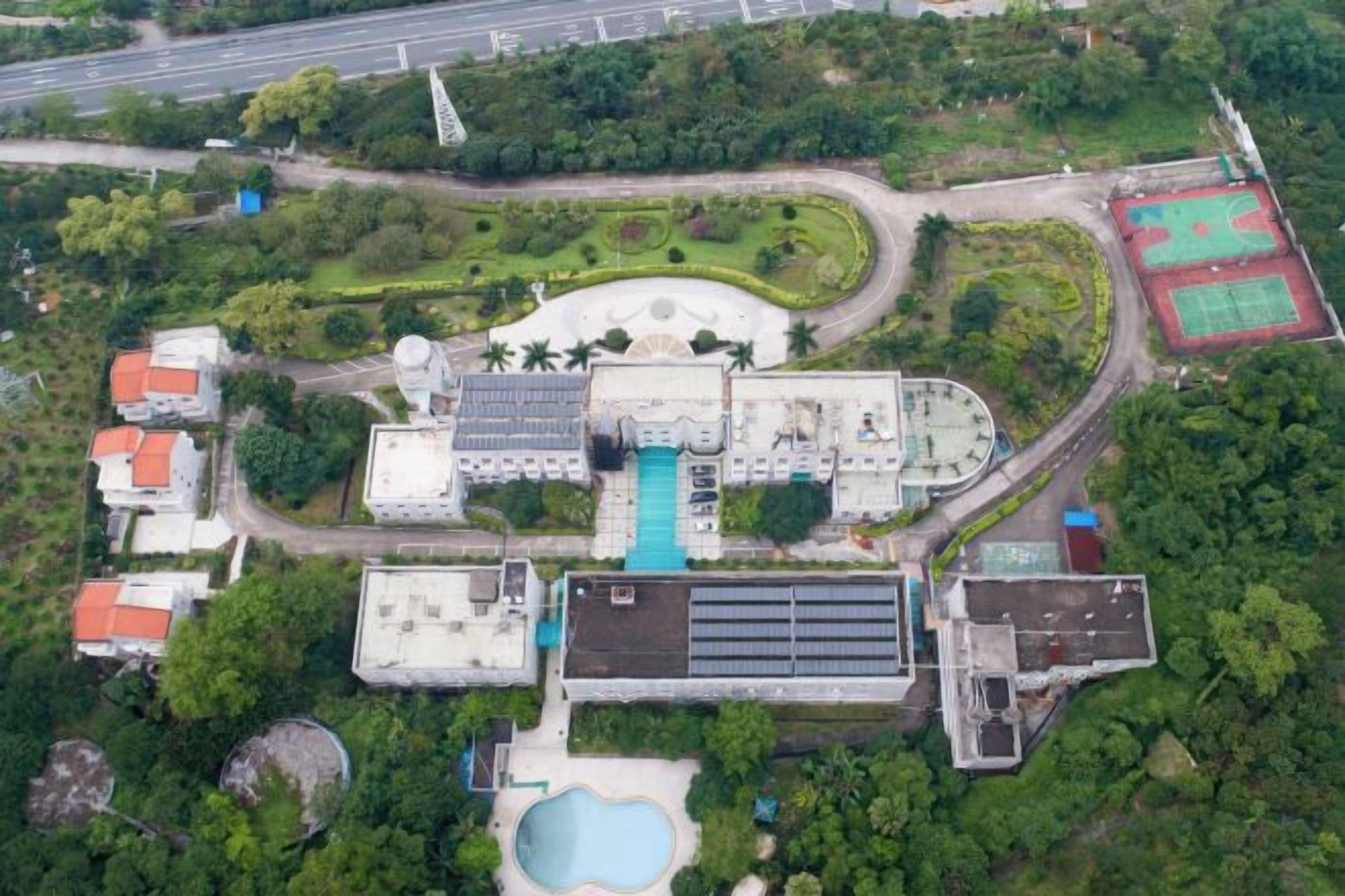 Vista aérea de un complejo con varias construcciones, piscina y follaje circundante.