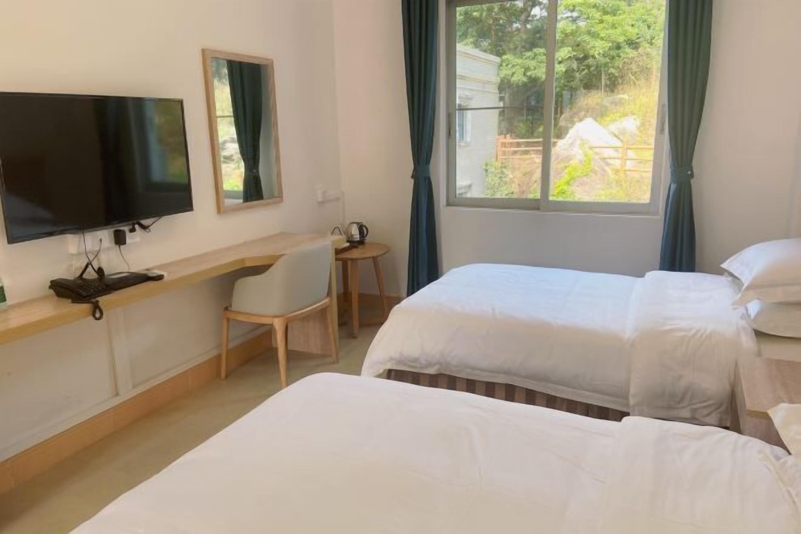 A hotel room with two beds, a desk with a chair, a television, and a window with curtains.