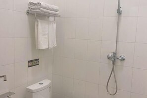 A bathroom with a toilet, a towel rack with folded towels, and a shower with a handheld showerhead.