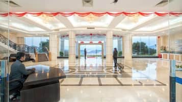 A spacious lobby with a reception desk, a staircase, and a large window offering a view.