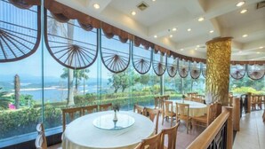 Un restaurant avec des tables et des chaises rondes, de grandes fenêtres ornées de motifs décoratifs et une vue sur la mer.