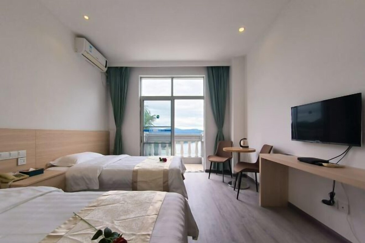 A hotel room with two beds, a TV, a desk, and a balcony with a view.