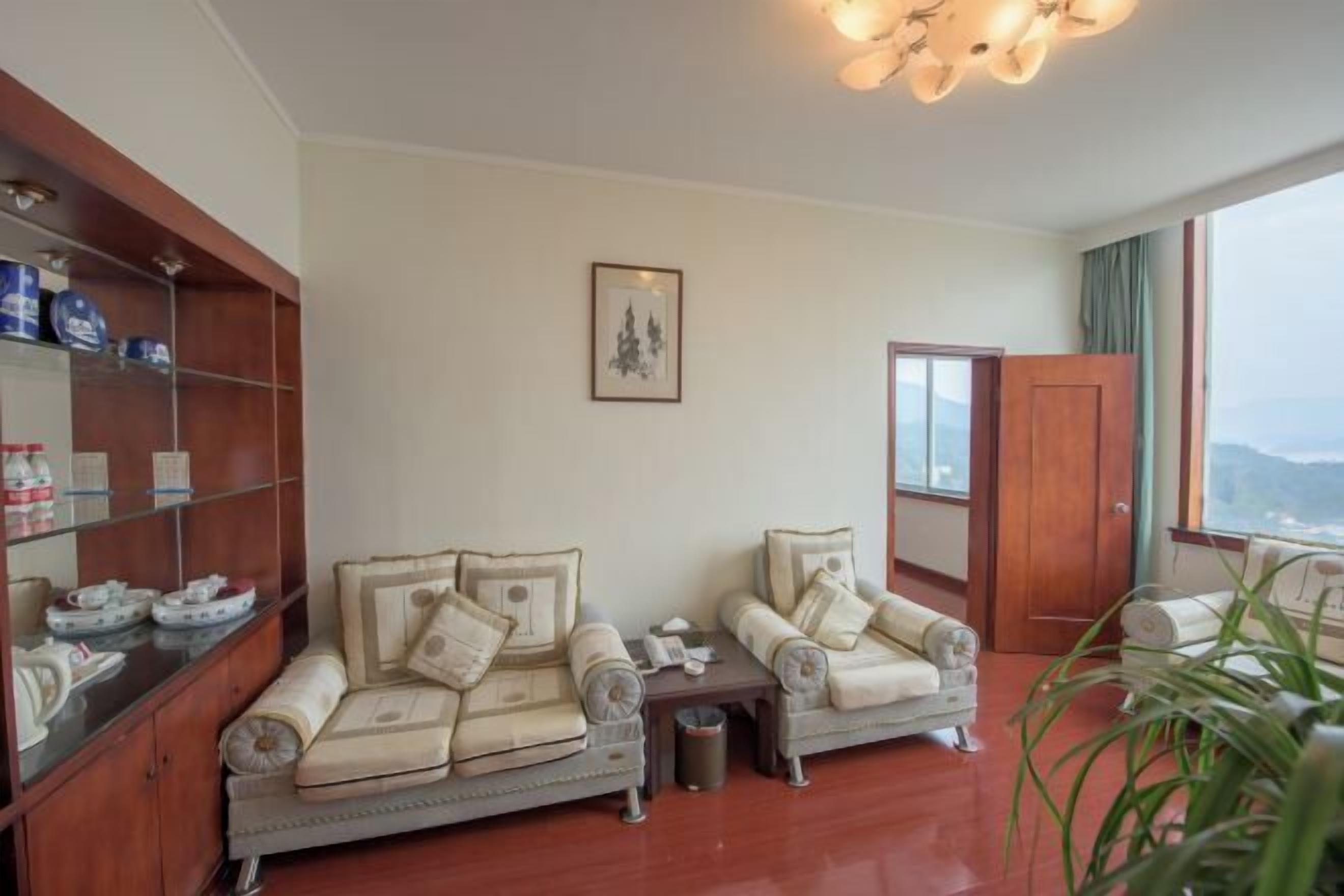 A room with two sofas, a wooden cabinet with kitchen items, a framed picture on the wall, and a view through a window.