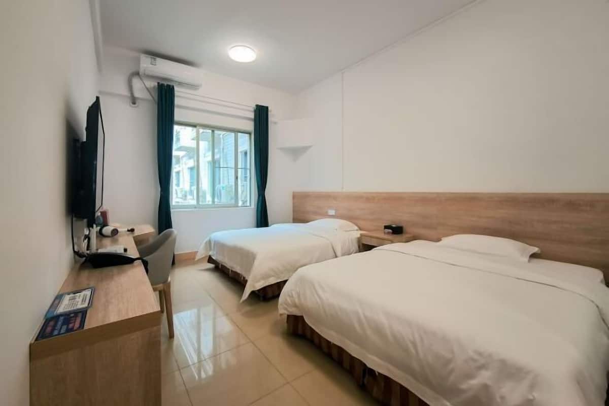 Une chambre d’hôtel avec deux lits, un bureau, une chaise, une télévision et une fenêtre avec des rideaux.