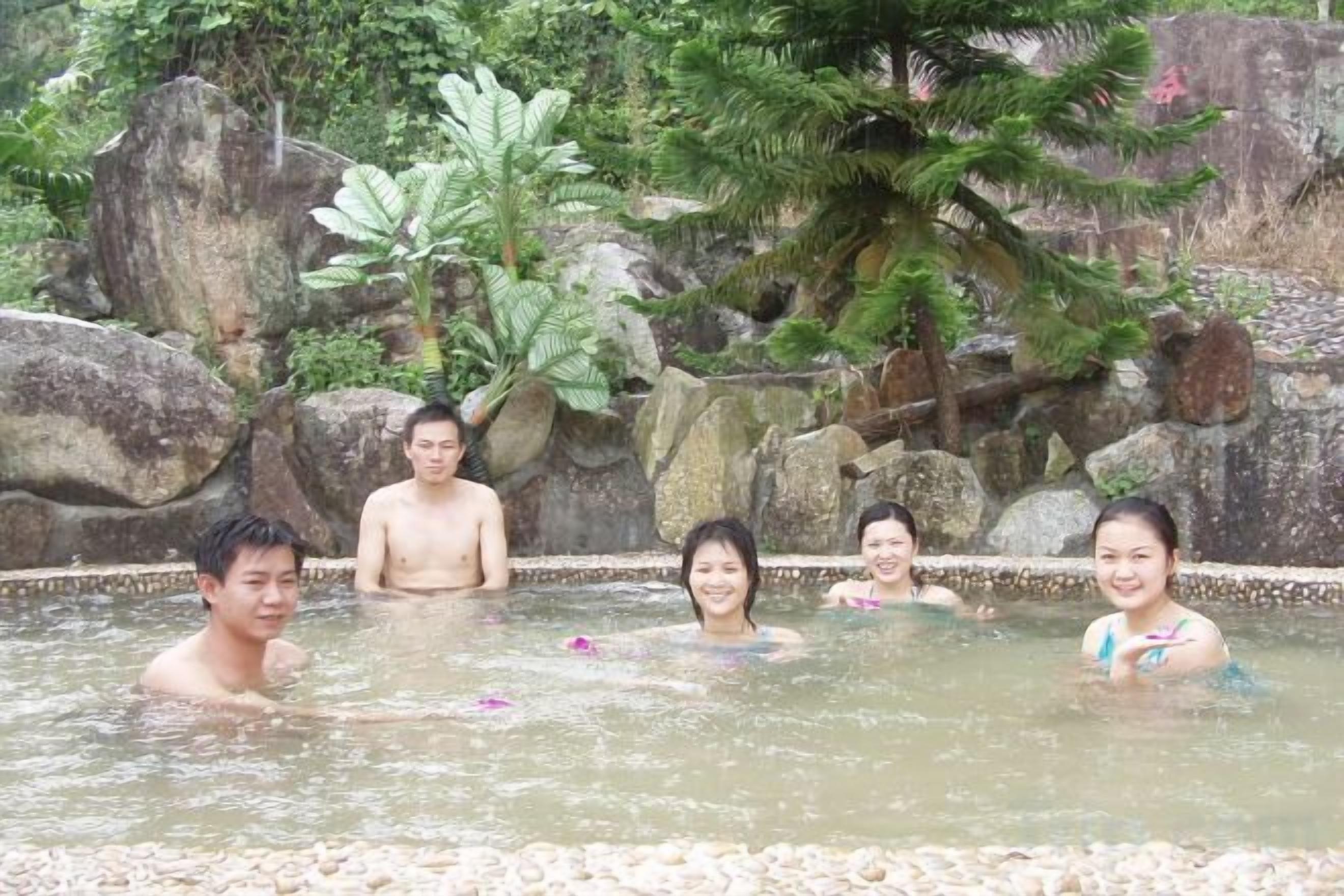 A group of people in a natural pool with rocks and greenery in the background.
