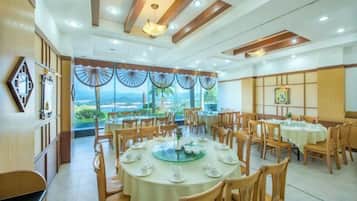 A restaurant with multiple round tables, wooden chairs, and a view of the outdoors.