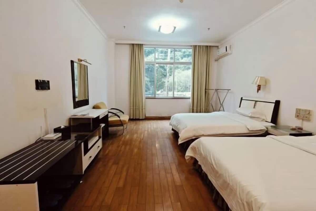 Une chambre d’hôtel avec deux lits, un bureau, une chaise, un miroir et une fenêtre avec des rideaux.