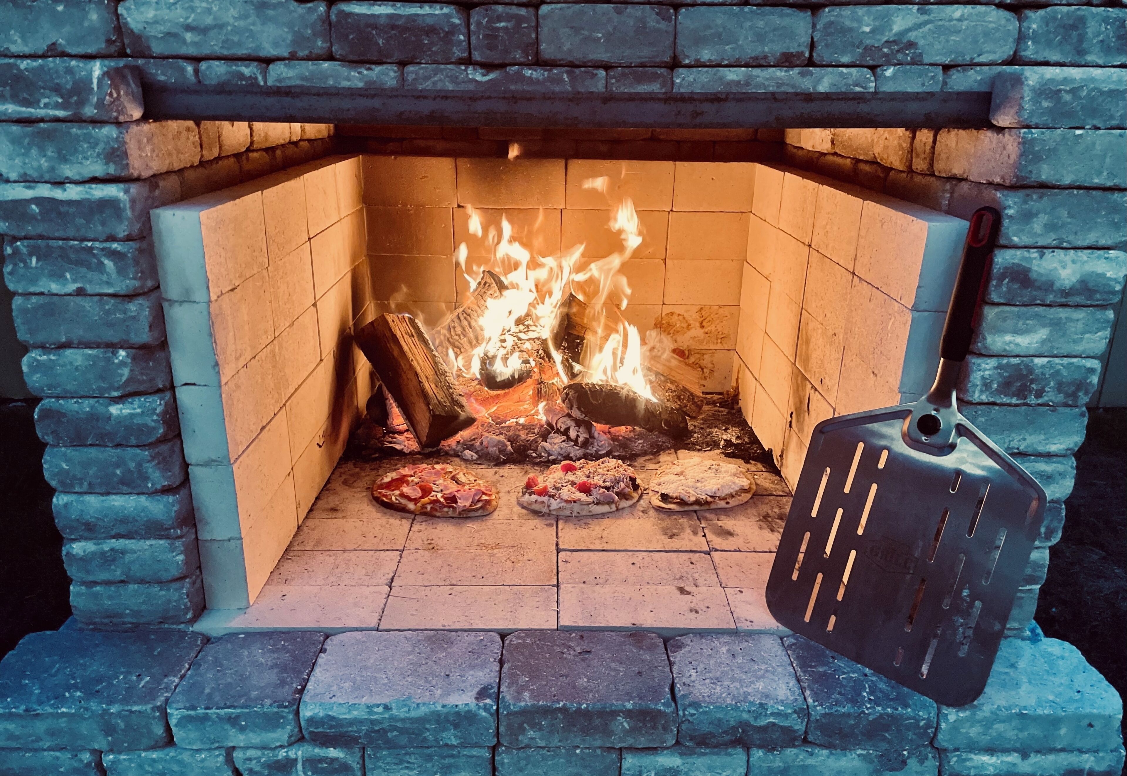 En tegelbeklädd öppen spis med en pizzasten och en pizzaspade.