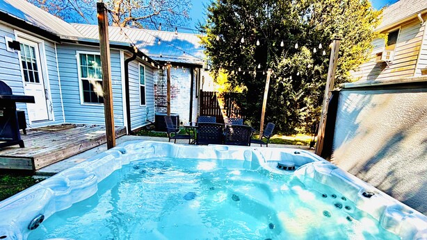 A hot tub in a backyard with a wooden deck, chairs, and a house in the background.