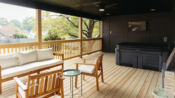 En overdækket terrasse med træmøbler, et spabad og udsigt over det omkringliggende landskab.