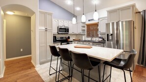 Une cuisine moderne avec des meubles blancs, des appareils en acier inoxydable et un îlot central doté de tabourets de bar.