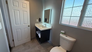 A bathroom with a white toilet, a sink with a mirror above it, and a window with a frosted glass design. - Travel Inn (Greenfield)