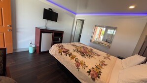 A bedroom with a bed, a television, a small refrigerator, a trash bin, and a mirror on the wall. - Travel Inn (Greenfield)