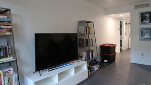 A living room with a flat-screen TV on a white entertainment unit, a bookshelf, and a black storage bin. - Comfortable 1 bdrm with a office Nook (Las Vegas)