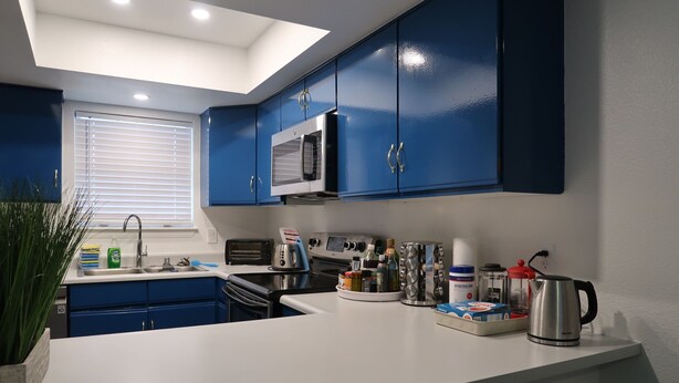 A modern kitchen with blue cabinets, a microwave, stove, and various kitchen appliances. - Comfortable 1 bdrm with a office Nook (Las Vegas)