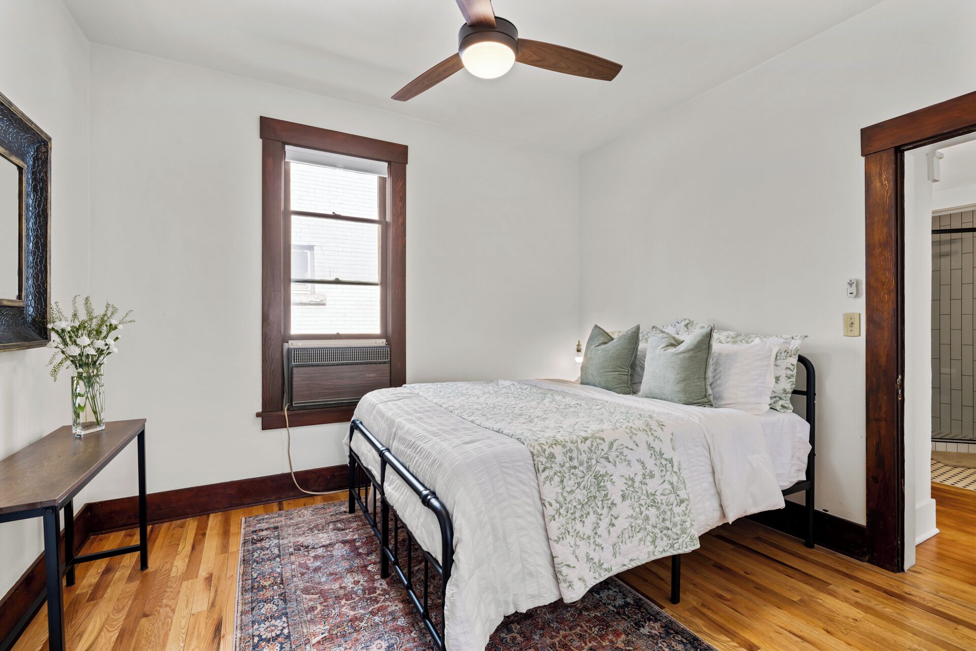 Une chambre à coucher comprenant un lit, un ventilateur de plafond, une fenêtre, une table de chevet et une commode.